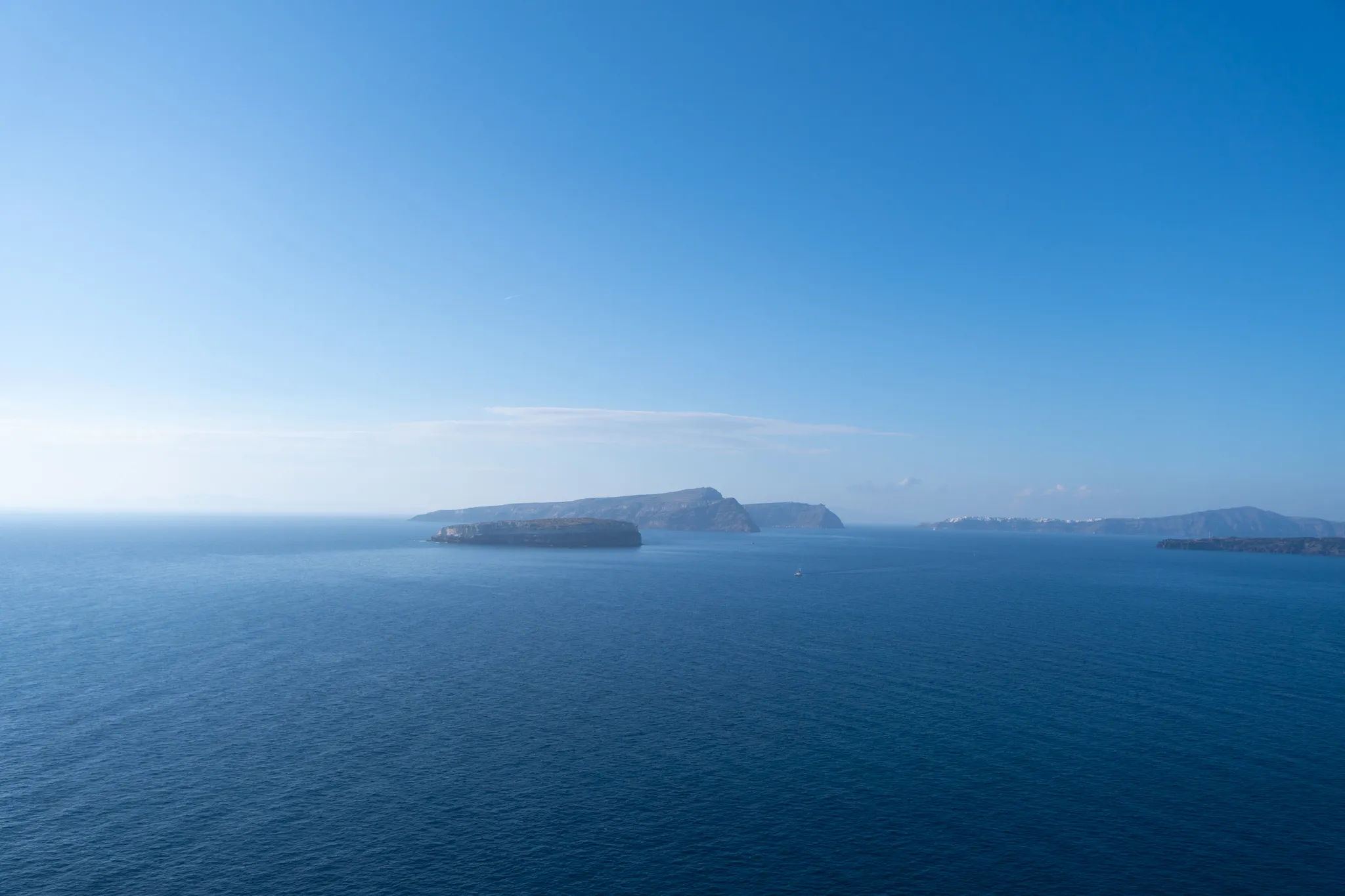 Deep blue sea under a clear sky, with the islands of the Santorini caldera on the horizon