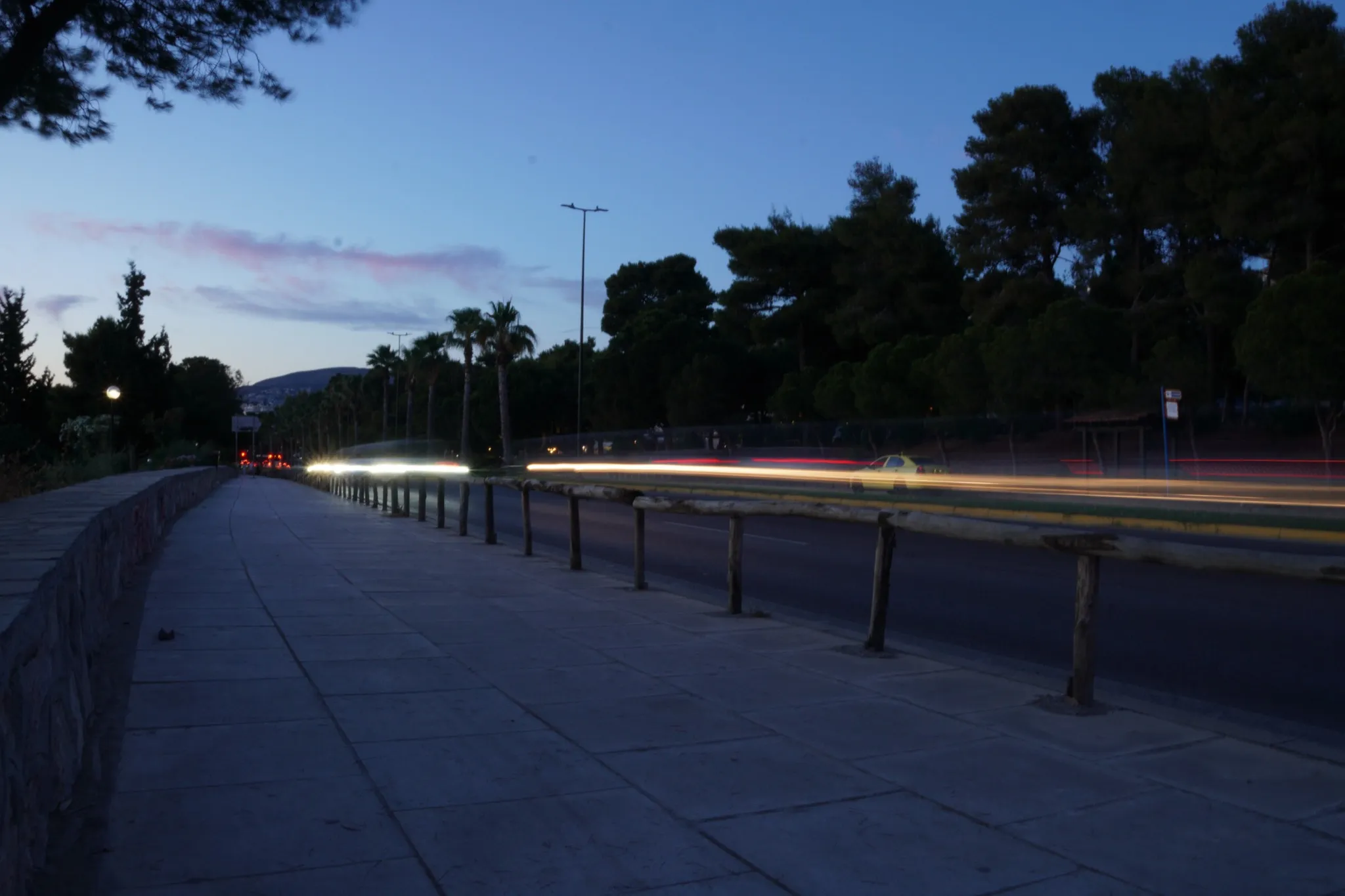 A pavement beside a road at dusk, headlights drawn into long streaks by a slow shutter