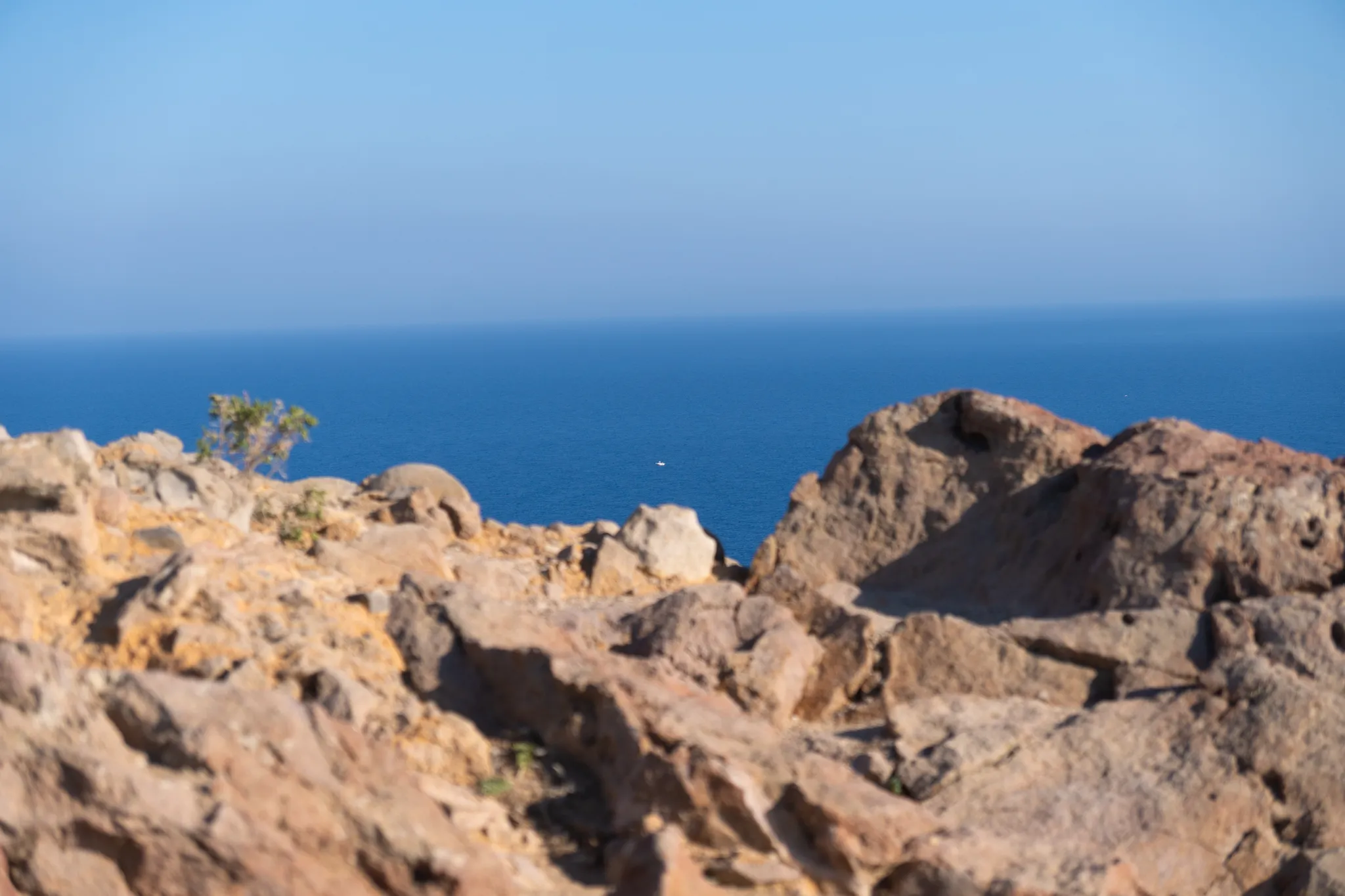 A sunlit rocky headland in soft focus, a single boat far out on the water beyond it