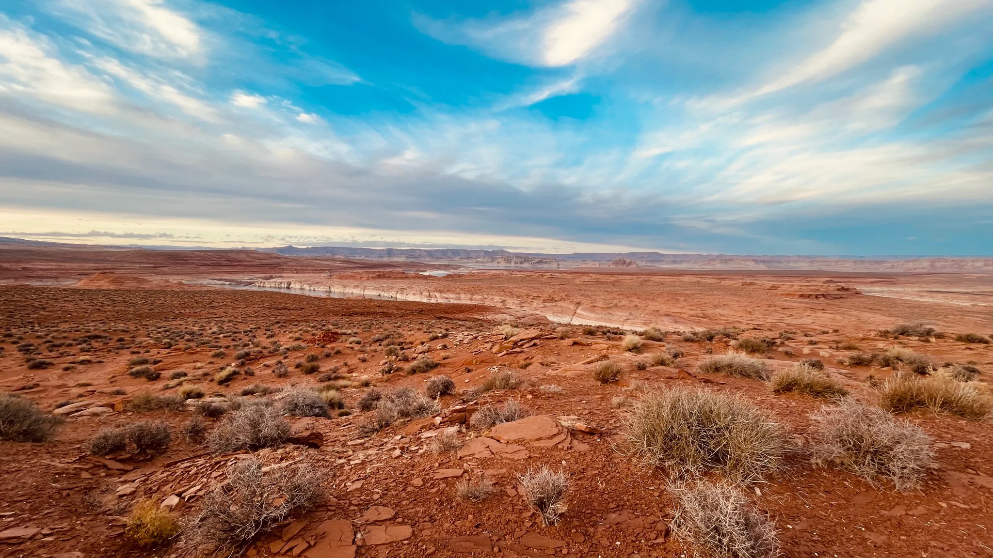 Red desert scrub in the foreground opening onto a wide lake and distant mesas
